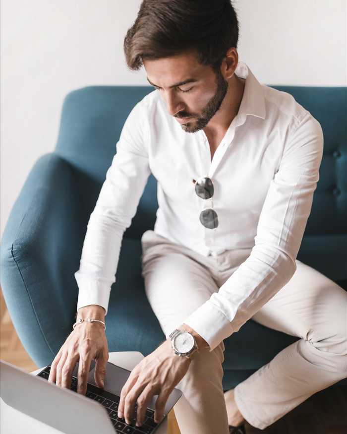 A man in a white shirt typing on a laptop on a teal sofa, seen from above