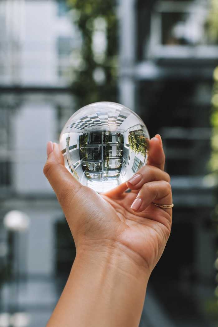 A hand holding a clear crystal ball that reflects a building