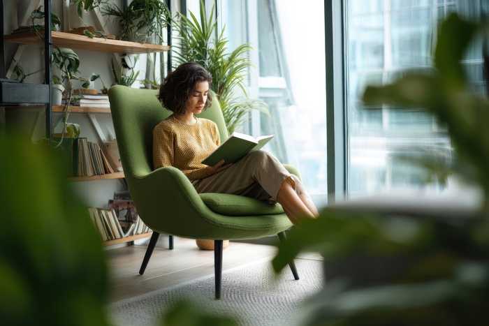 A woman reading a book in a green armchair among plants